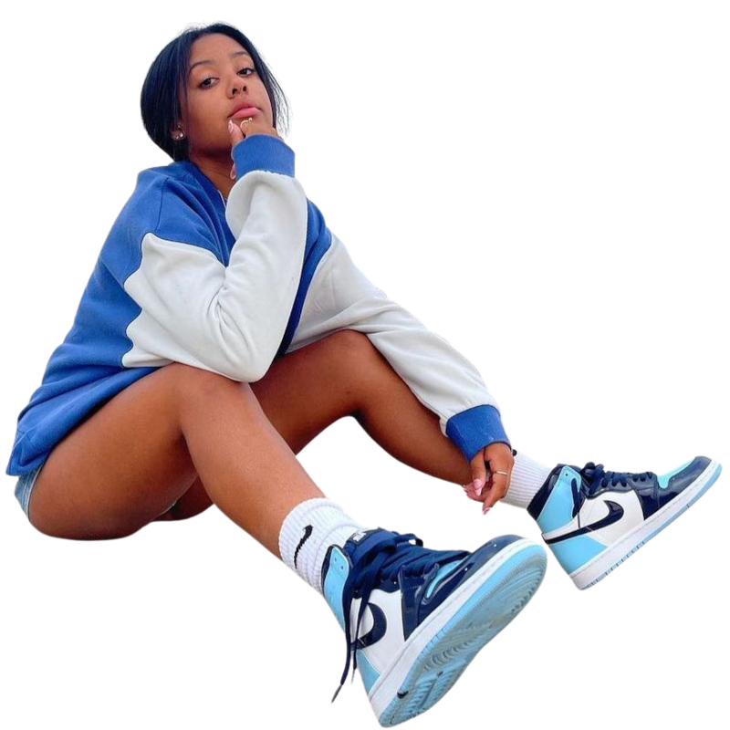 Een sportmeisje die een blauw-wit jasje, sportschoenen en witte sokken draagt, zit op de grond met één been gestrekt en de hand onder de kin.