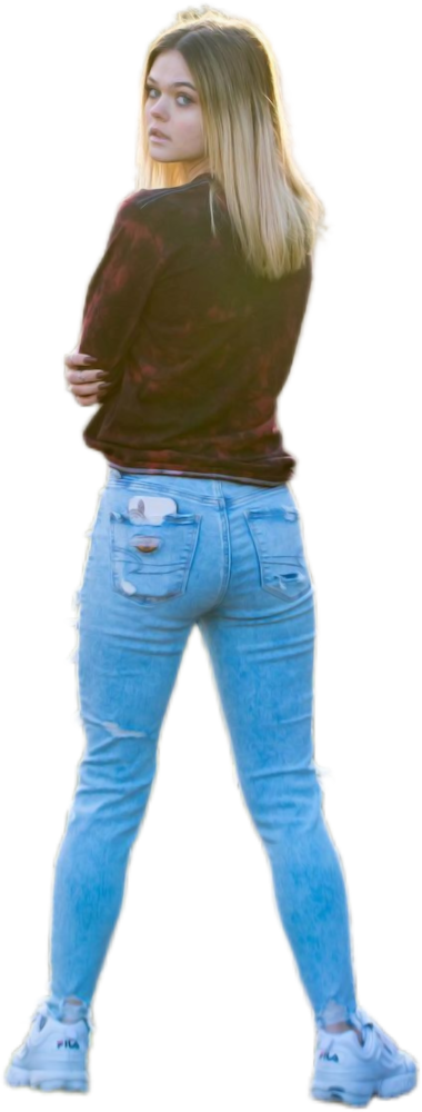 Een studente met lang haar staat afgewend en kijkt over haar schouder. Ze draagt een donker topje met lange mouwen, een versleten lichtblauwe spijkerbroek en witte sneakers.