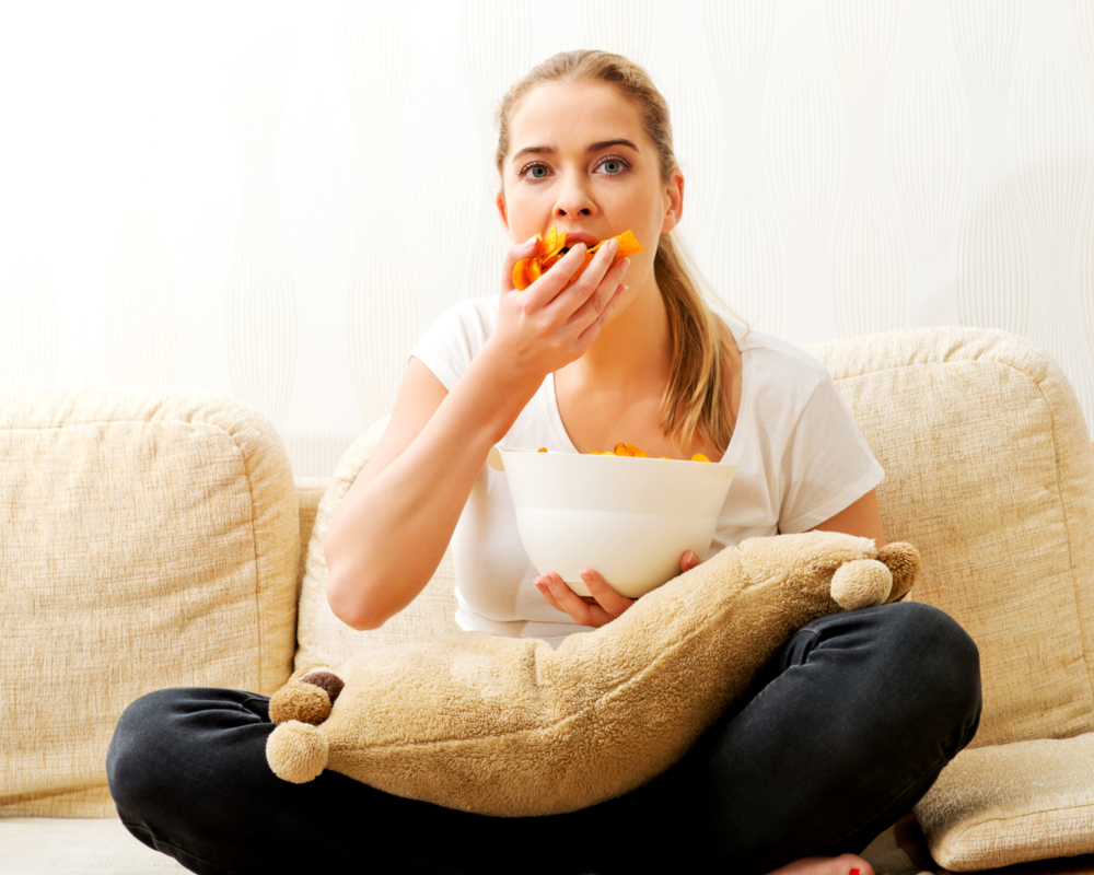 vreetbuiten Een persoon zit op een bank en eet uit een kom met gesneden mango's, terwijl hij een knuffel op schoot houdt.
