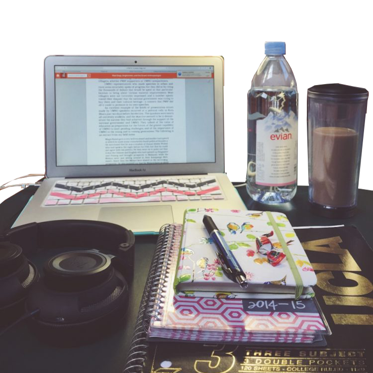 Een laptop met tekst naast een Evian-fles, koffiekopje, koptelefoon en stapel notitieboekjes met een pen in een studeerhoek.