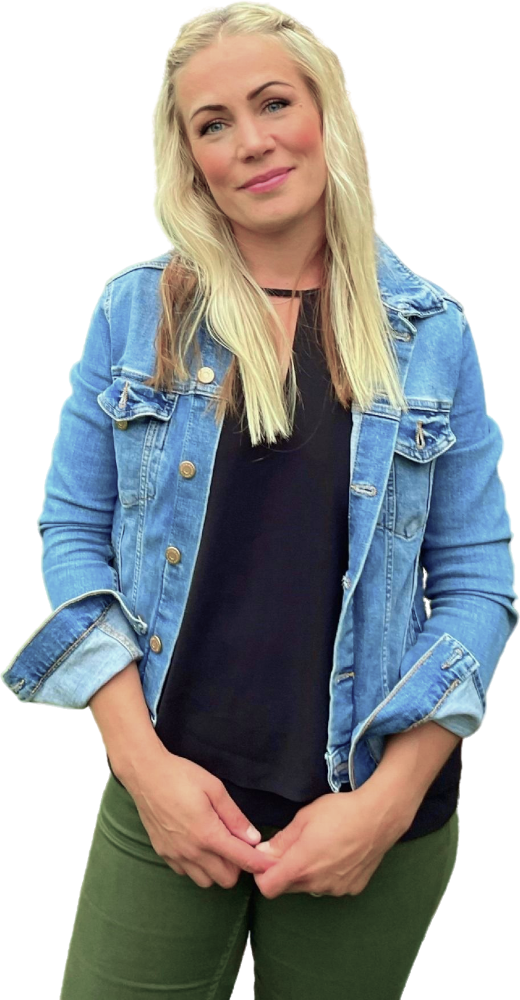 Een vrouw, gekleed in een zwart shirt, een groene broek en een spijkerjasje kijkt in de camera.