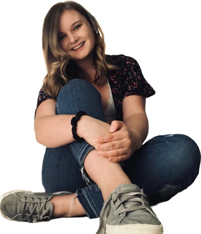 Een vrouw zit op de grond met ee knie opgetrokken en kijkt lachend in de camera.